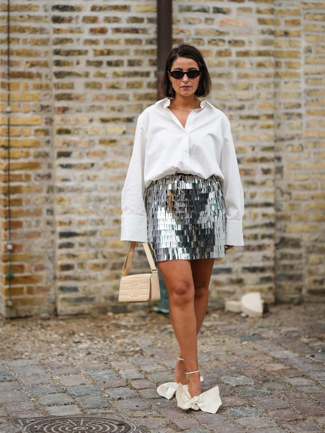 A Fashion Week guest styles a white shirt with a silver textured mini skirt 