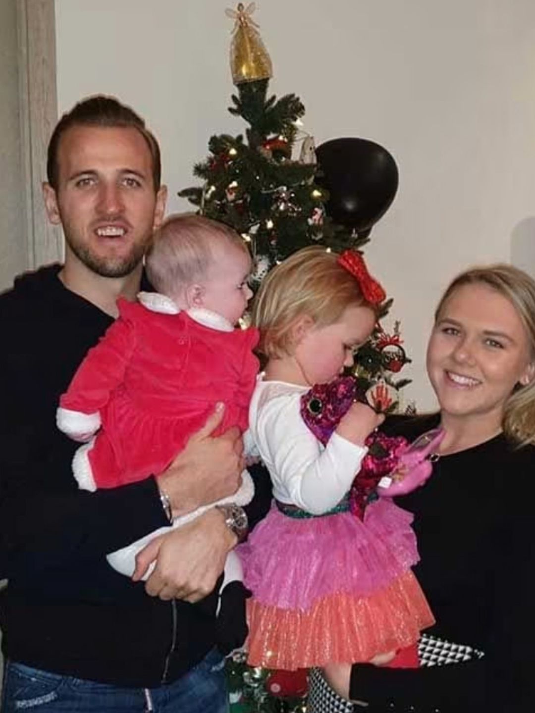 Harry Kane and his wife carrying their two daughters in front of a Christmas tree