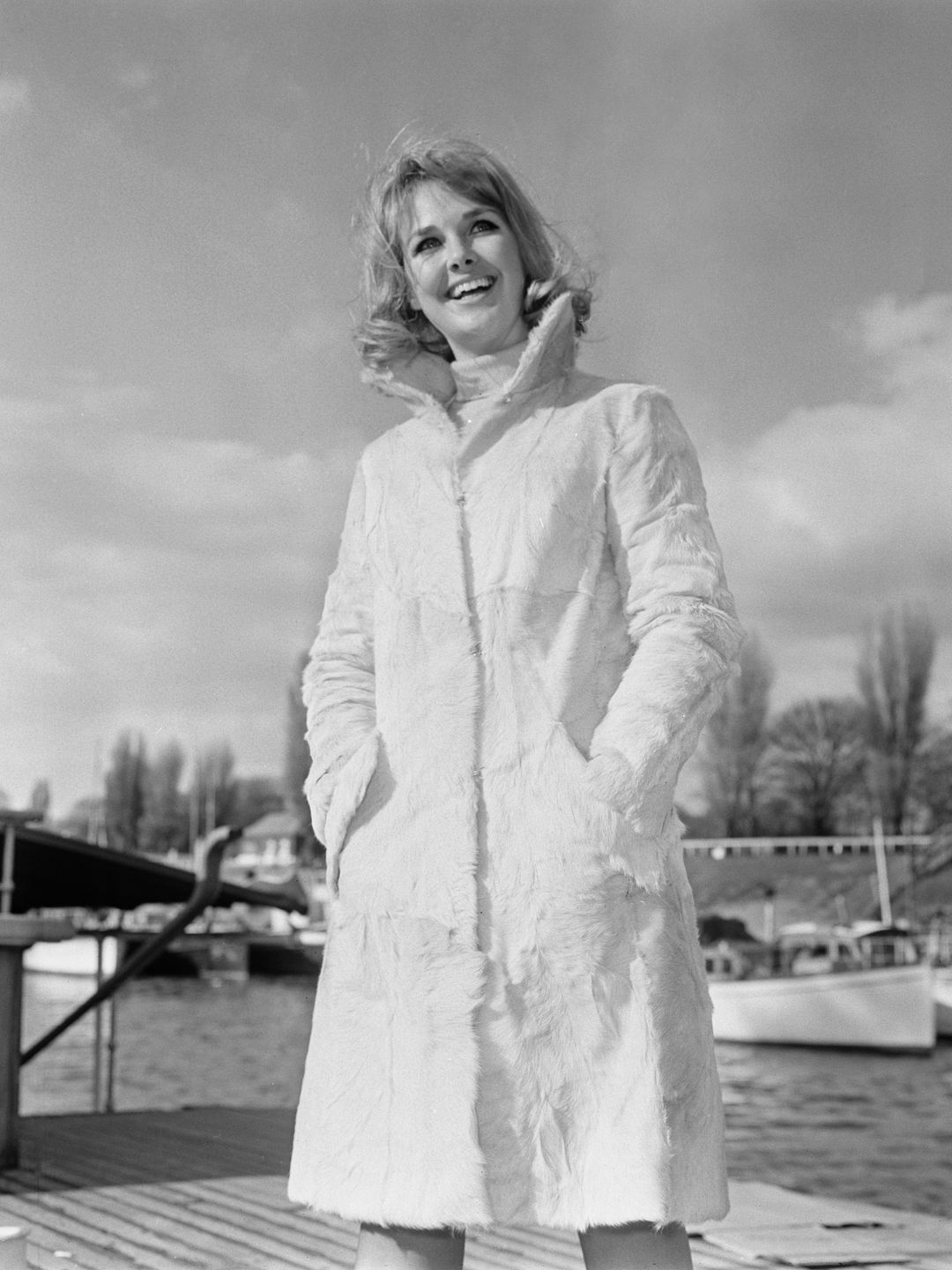 actress posing by river in coat 