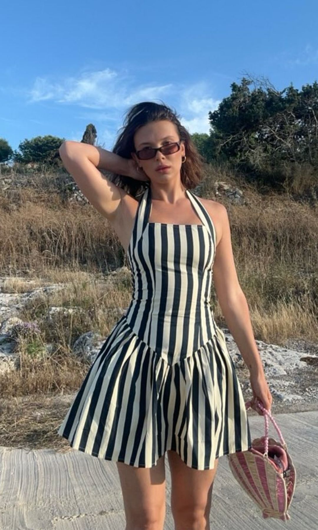 Millie Bobby Brown poses for a photo on the beach in a stripey mini dress