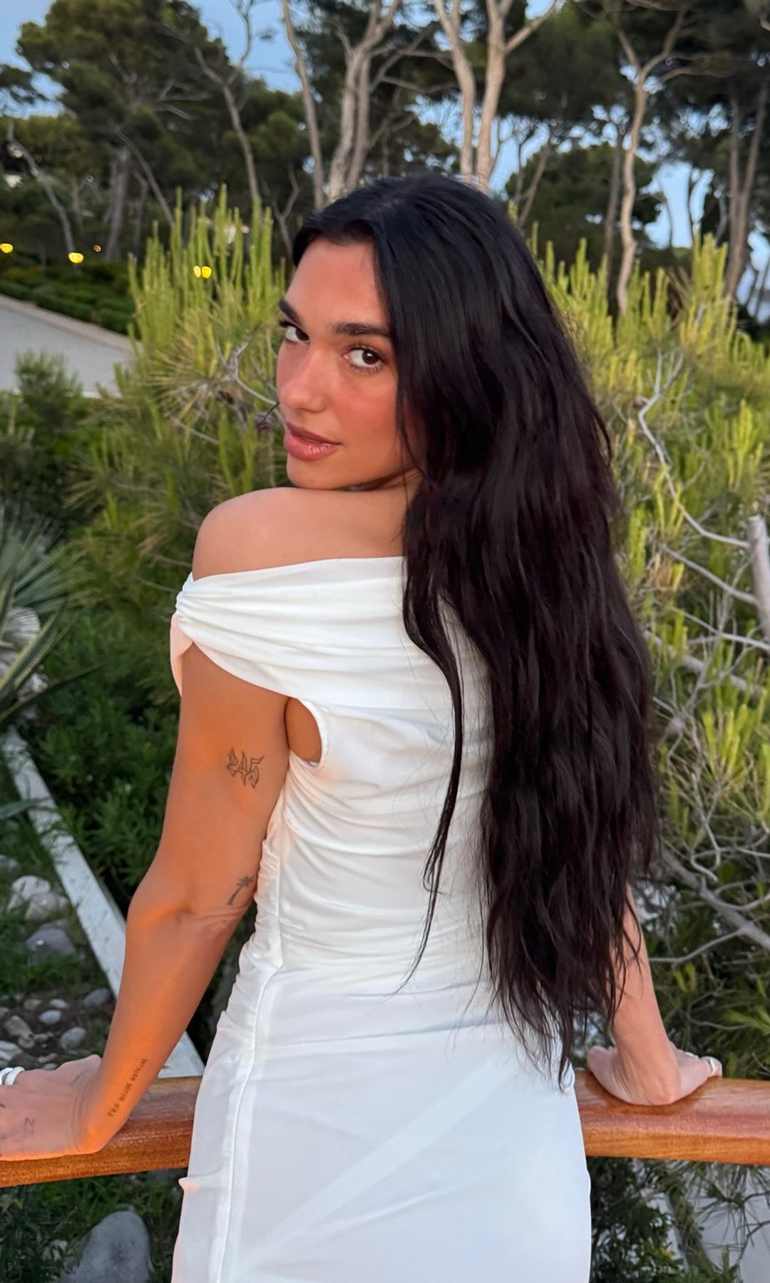 Dua Lipa poses for a photo in a white dress while on holiday with her family
