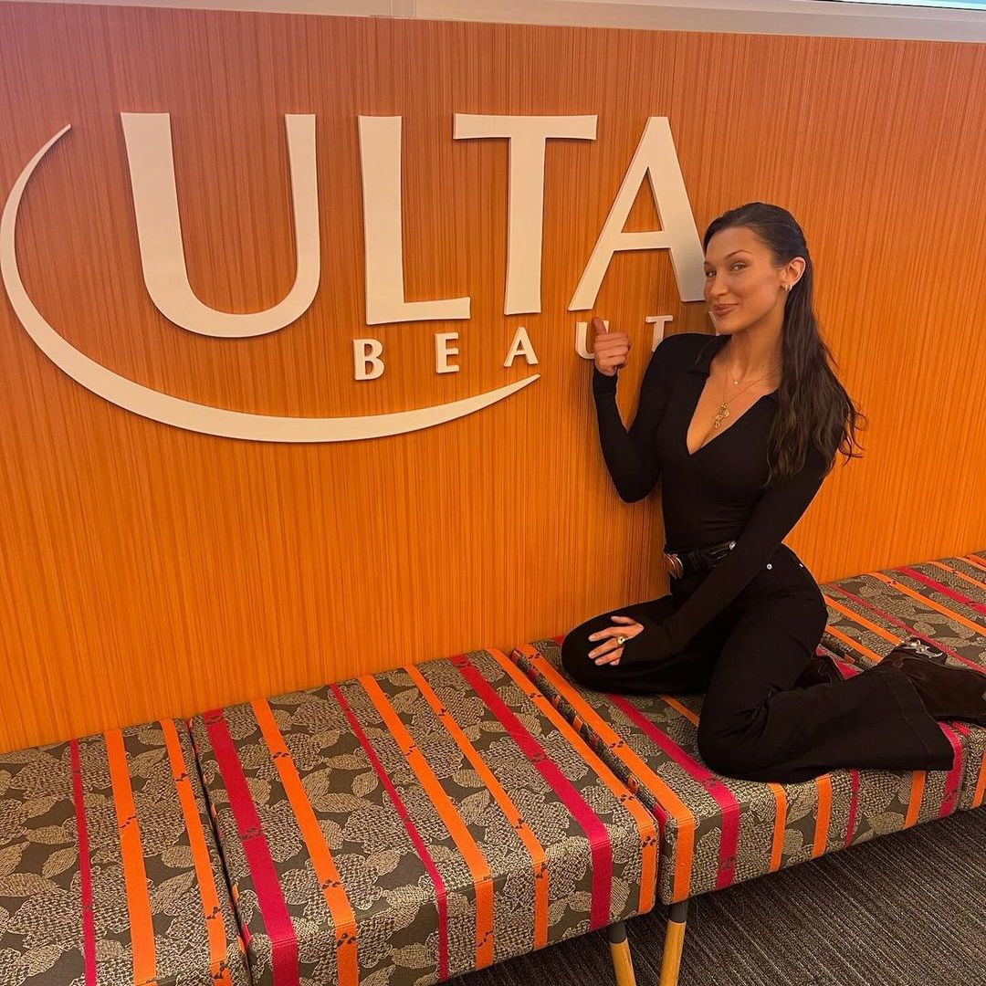 Bella Hadid kneeling next to an Ulta Beauty sign 