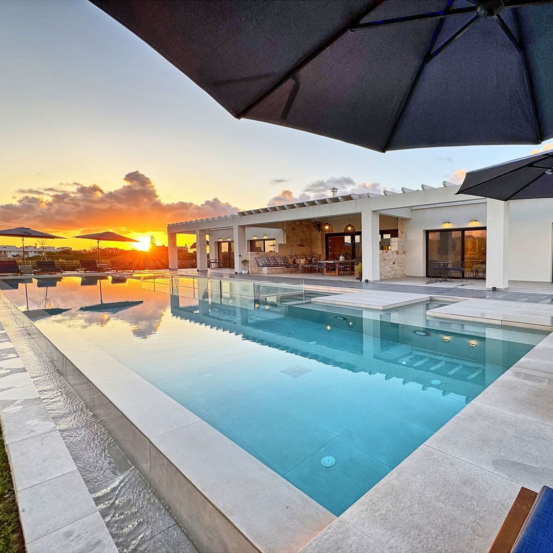 outdoor pool area with loungers and large luxury terrace at villa with sunset in background