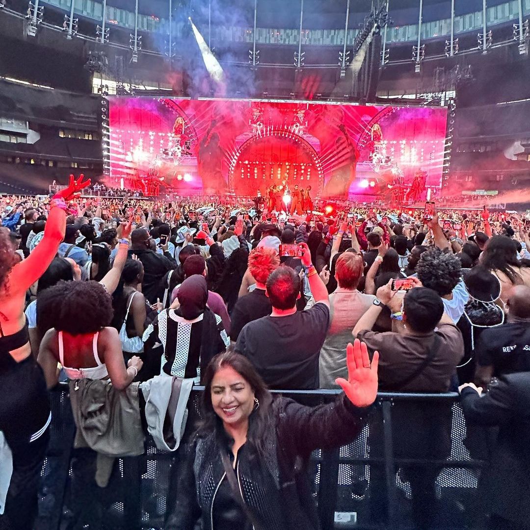 Priyanka's mom posing with her arms up enjoying the music with the stage and crowd behind her