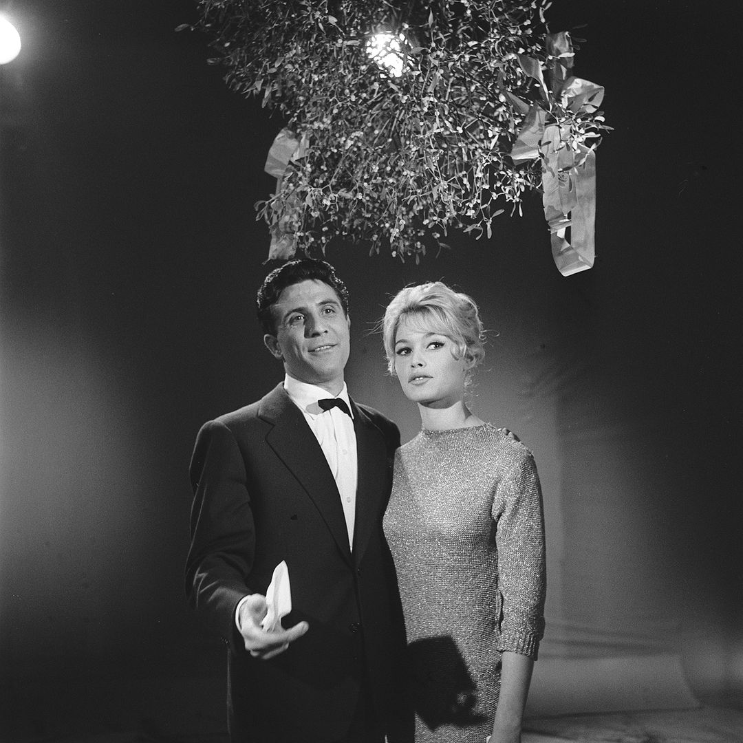 Brigitte Bardot and Gilbert Becaud under a bouquet of mistletoe present their wishes for year 1958, during the shooting of the program ""Parade of the end of year""