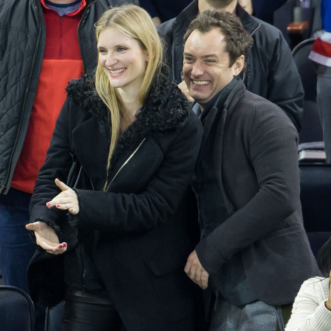 Jude Law and Phillipa Coan smiling while standing watching a sports game