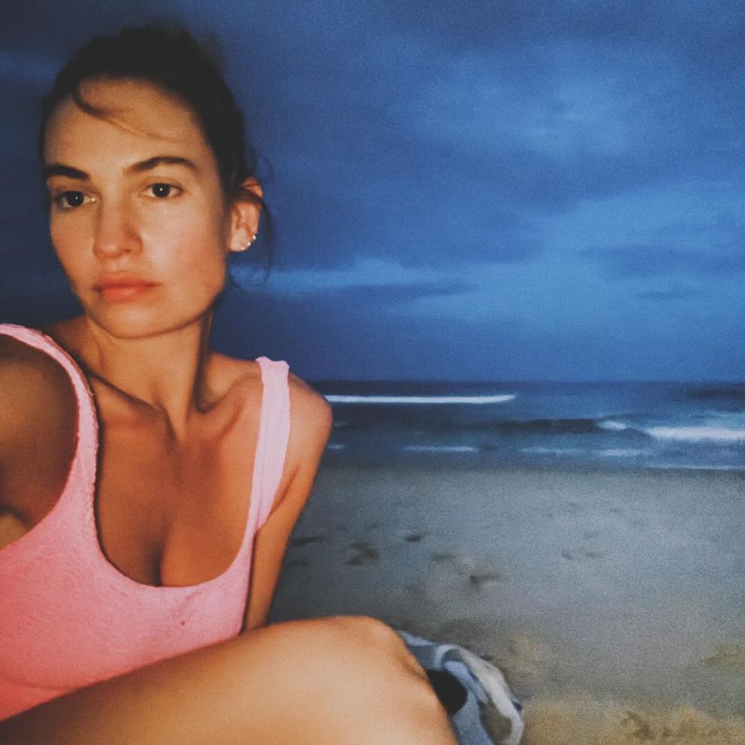 Lily James takes a selfie wearing a pink crinkle swimsuit on the beach