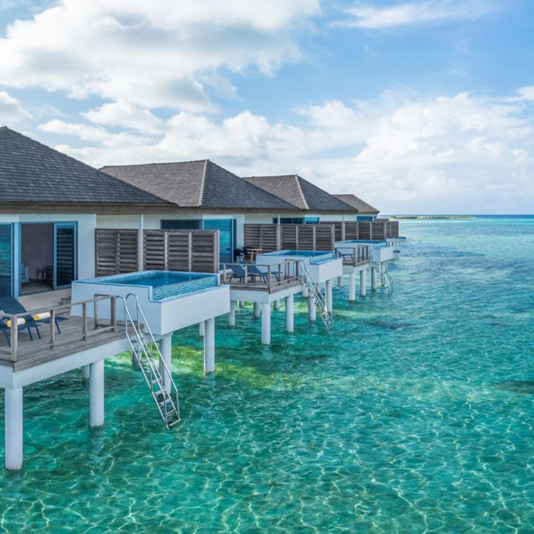 A series of overwater villas perched on stilts above crystal-clear turquoise water.