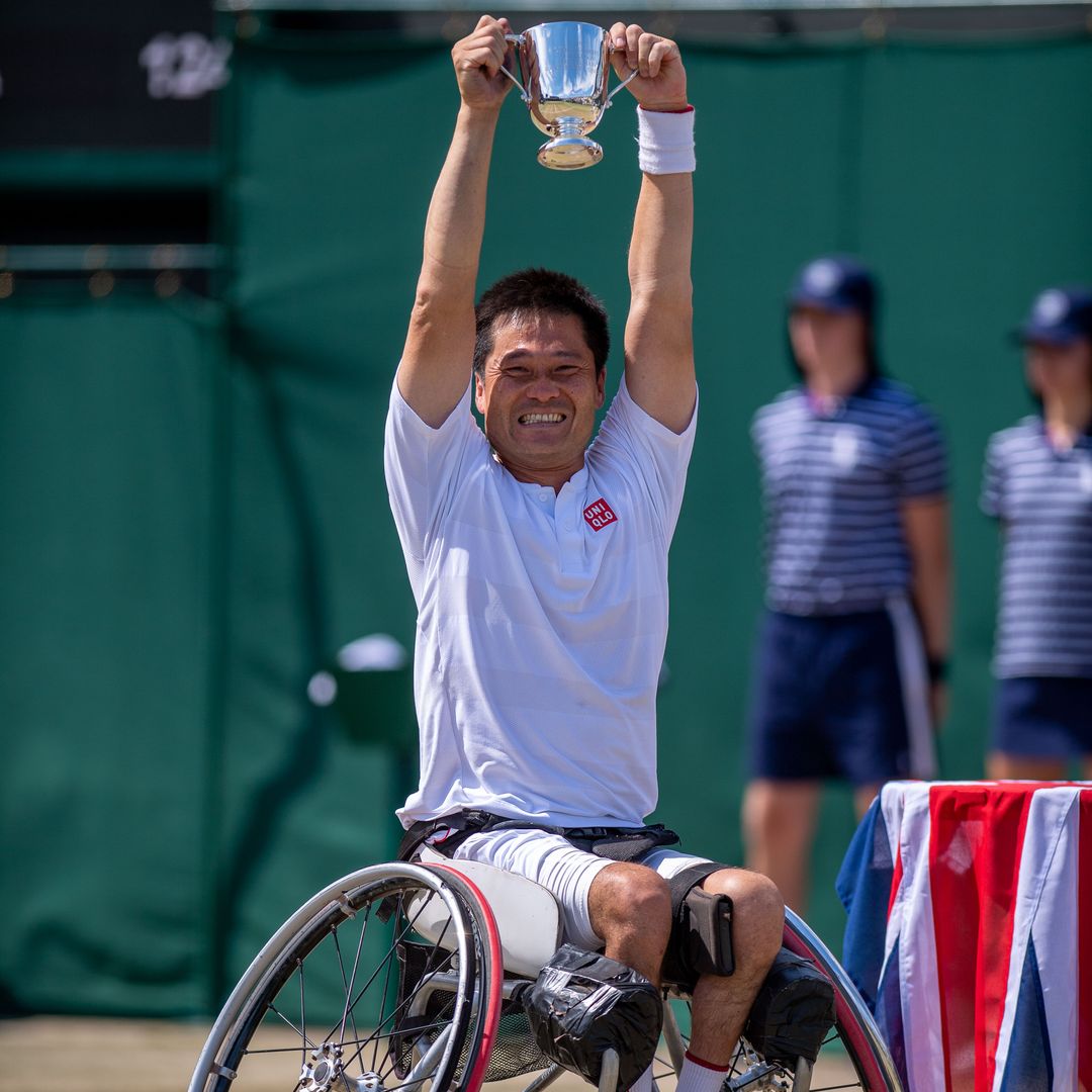 Shingo Kunieda holding a cup above his head, smiling. He is in a wheelchair.