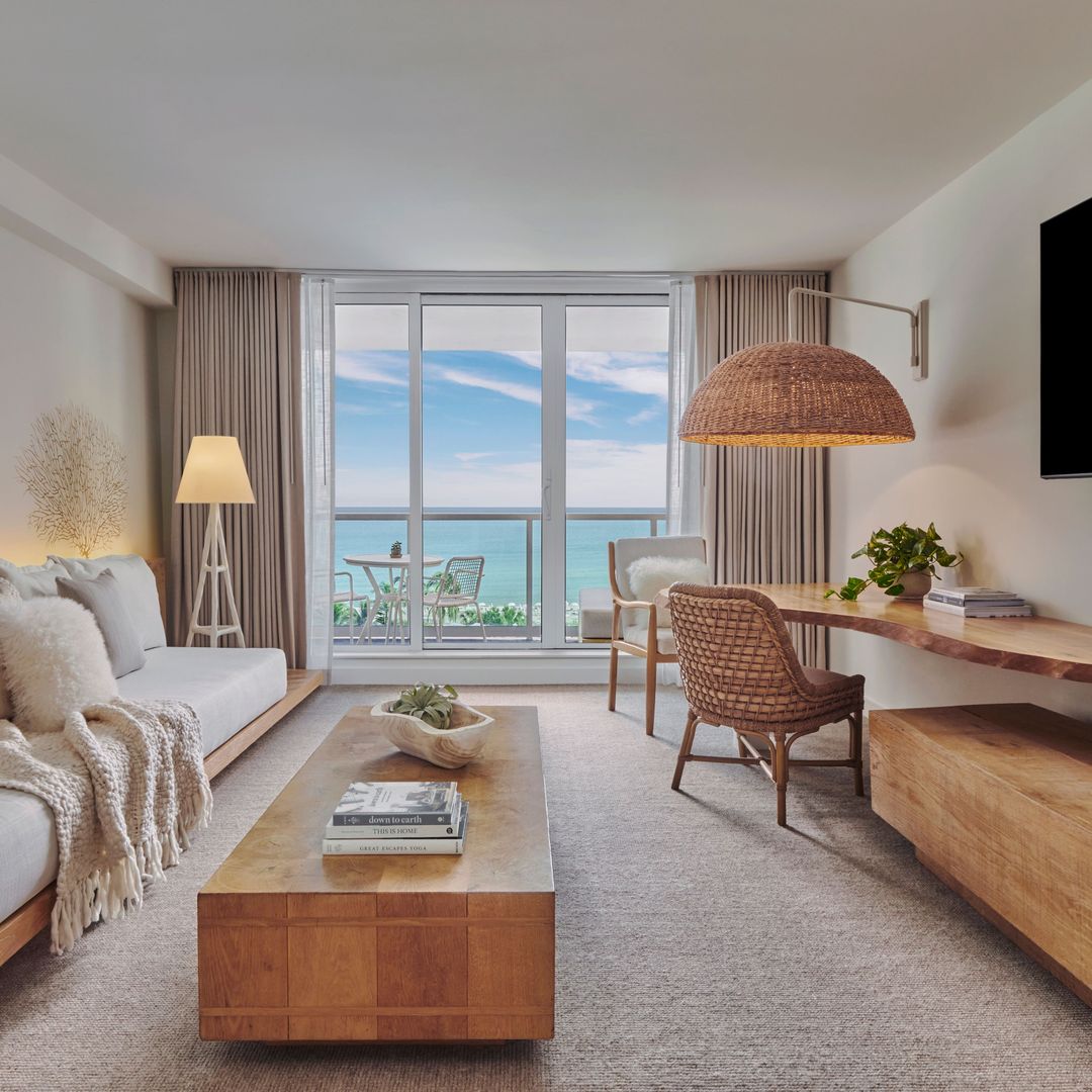A serene, modern hotel room with neutral tones and natural wood accents and a balcony view of the ocean