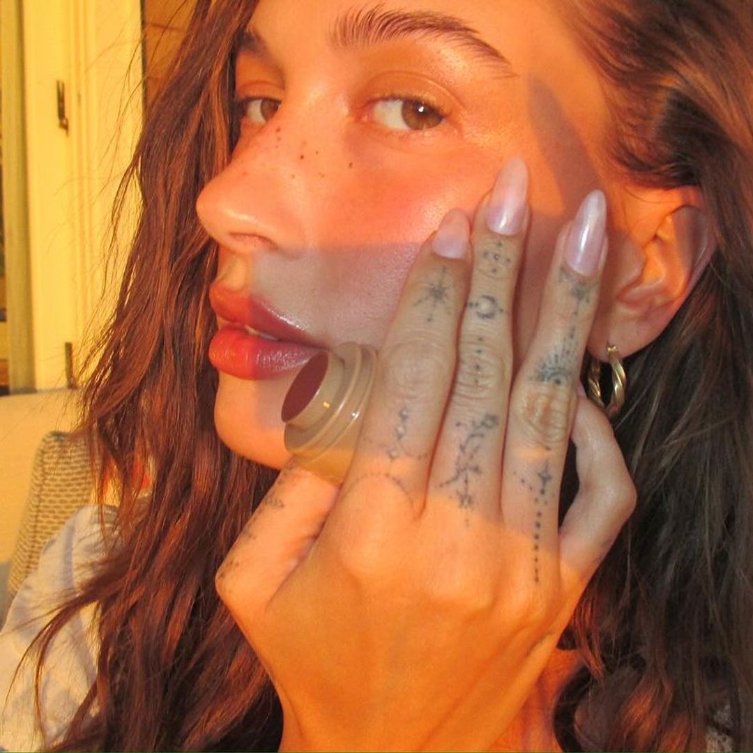 Hailey Bieber applying blush with her fingers in the sun