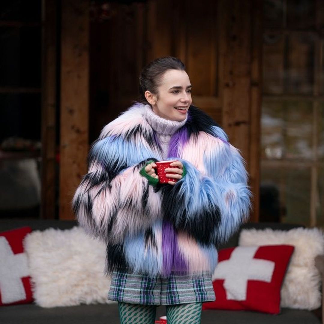 Lily Collins in a fur jacket holding a red mug