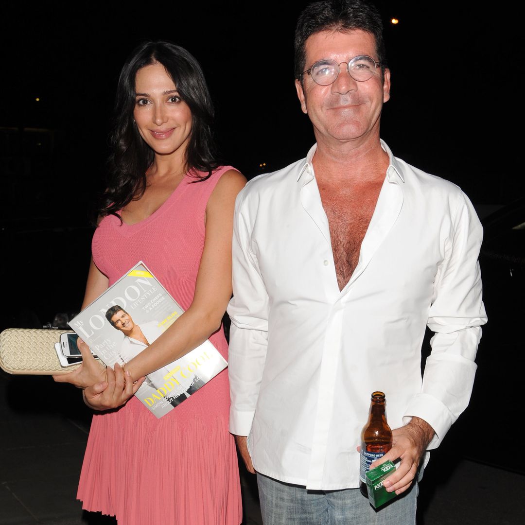 Lauren and Simon smiling at the camera, he is holding a bottle and she has a bag and a magazine