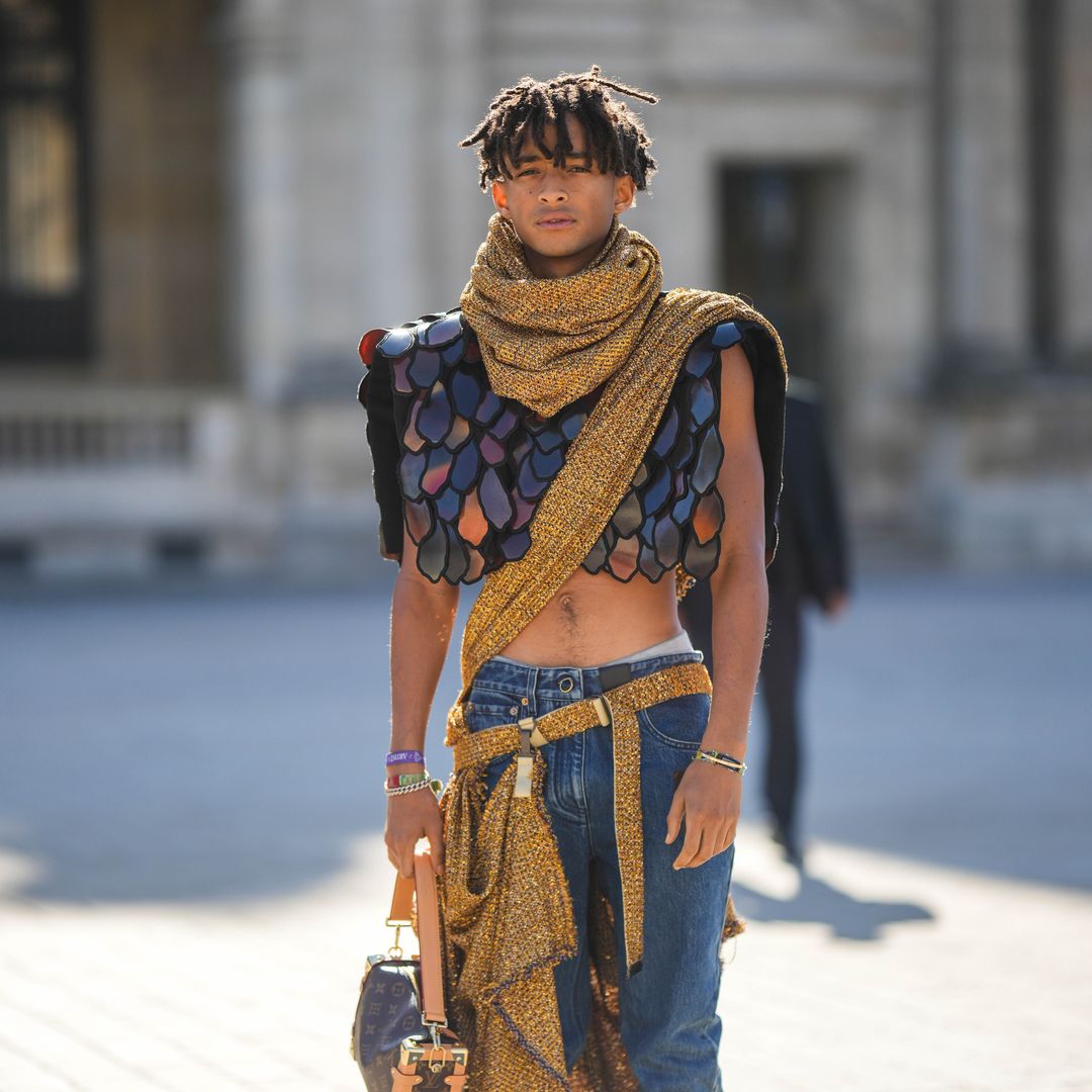 Jaden Smith wears a gold and black tweed with embroidered sequined scarf from Louis Vuitton, a gold and black tweed with embroidered sequined crossbody / belted long scarf, a black and burgundy embroidered yoke sleeveless / cropped top from Louis Vuitton, a brown LV monogram print pattern in coated canvas handbag from Louis Vuitton, navy blue denim large pants, a gold Love bracelet from Louis Vuitton, colored bracelets, white leather and pale gray sneakers from New Balance , outside Louis Vuitton, during Paris Fashion Week - Womenswear Spring/Summer 2023, on October 04, 2022 in Paris, France.