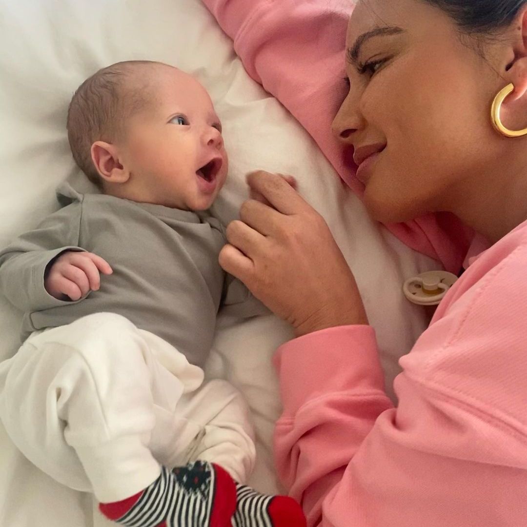 Olivia lying on a bed smiling and looking at a happy little baby Malcolm beside her