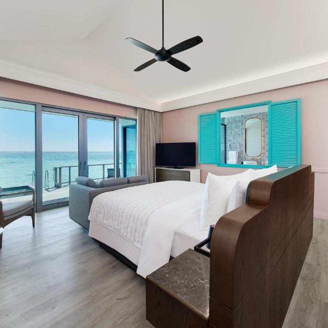 A bright, airy bedroom with floor-to-ceiling windows offering a view of the turquoise ocean.