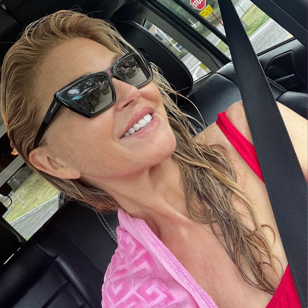 Christie smiling in a car selfie with sunglasses on and a pink towel on her shoulder