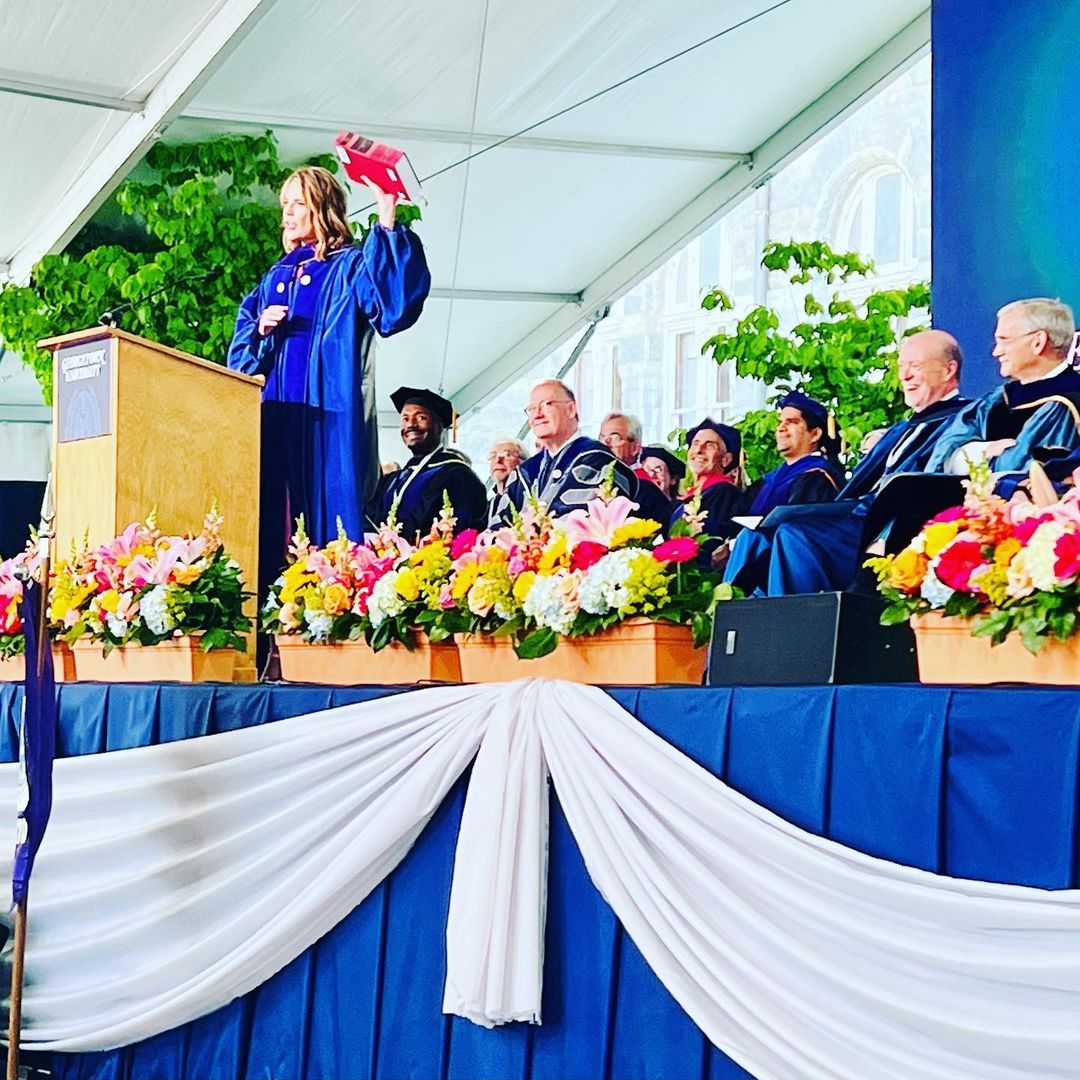 Savannah on stage holding up a large book while giving a commencement address at Georgetown Law