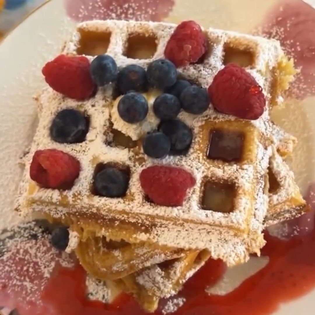 A plate of waffles with fruit and strawberry sauce