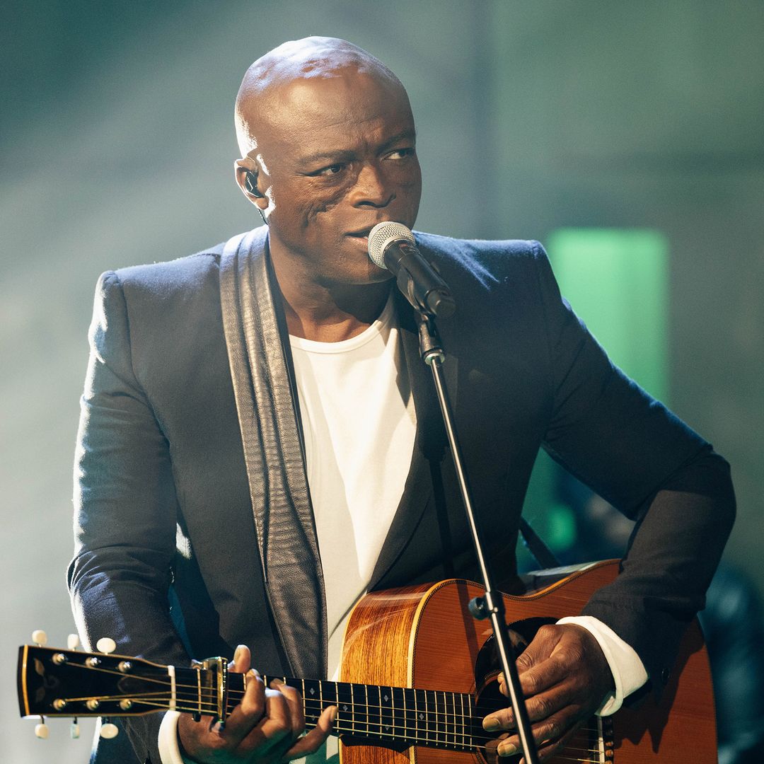 Seal performing on a stage with a guitar and singing into a microphone