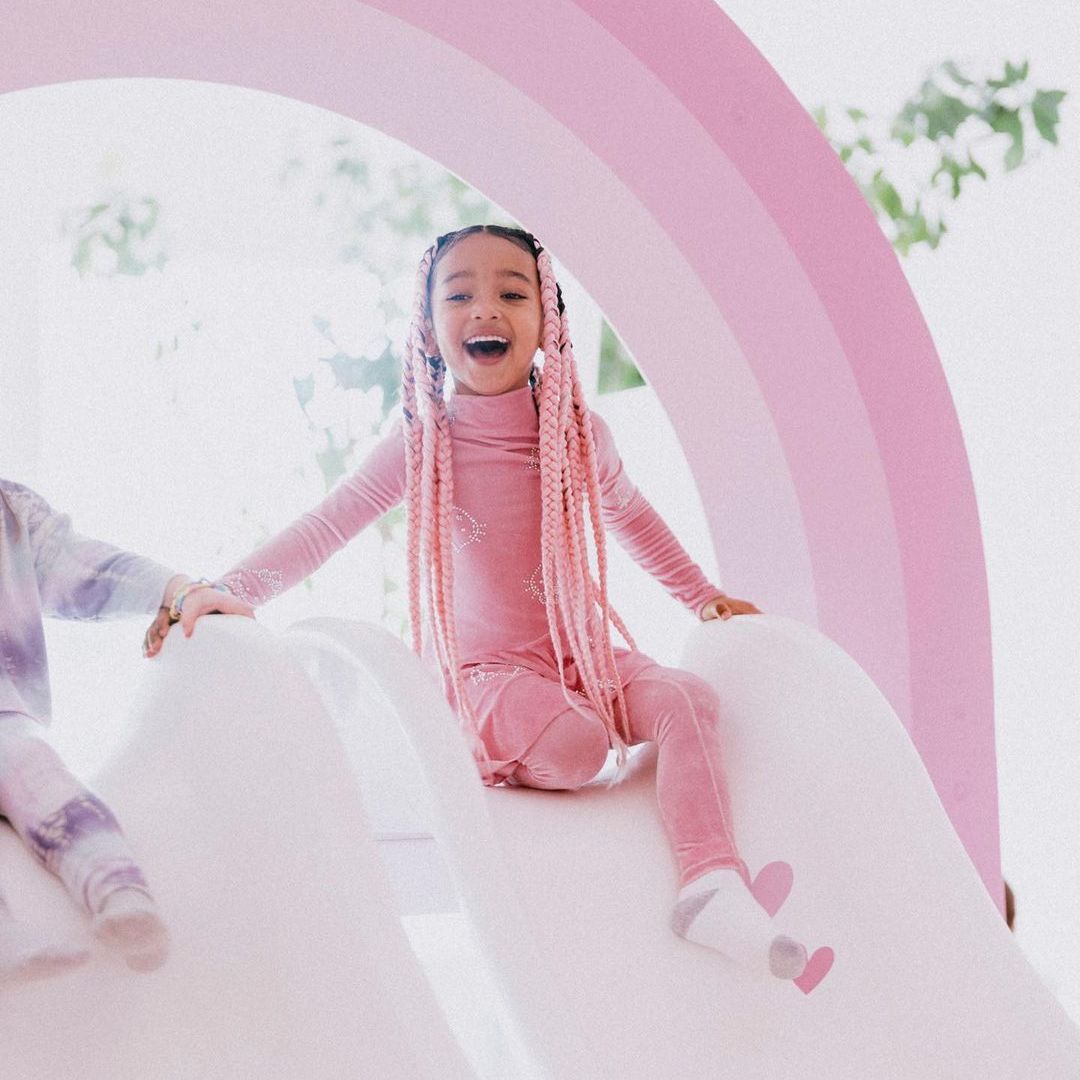 Chicago West beaming while wearing all pink, she is sat on a slide