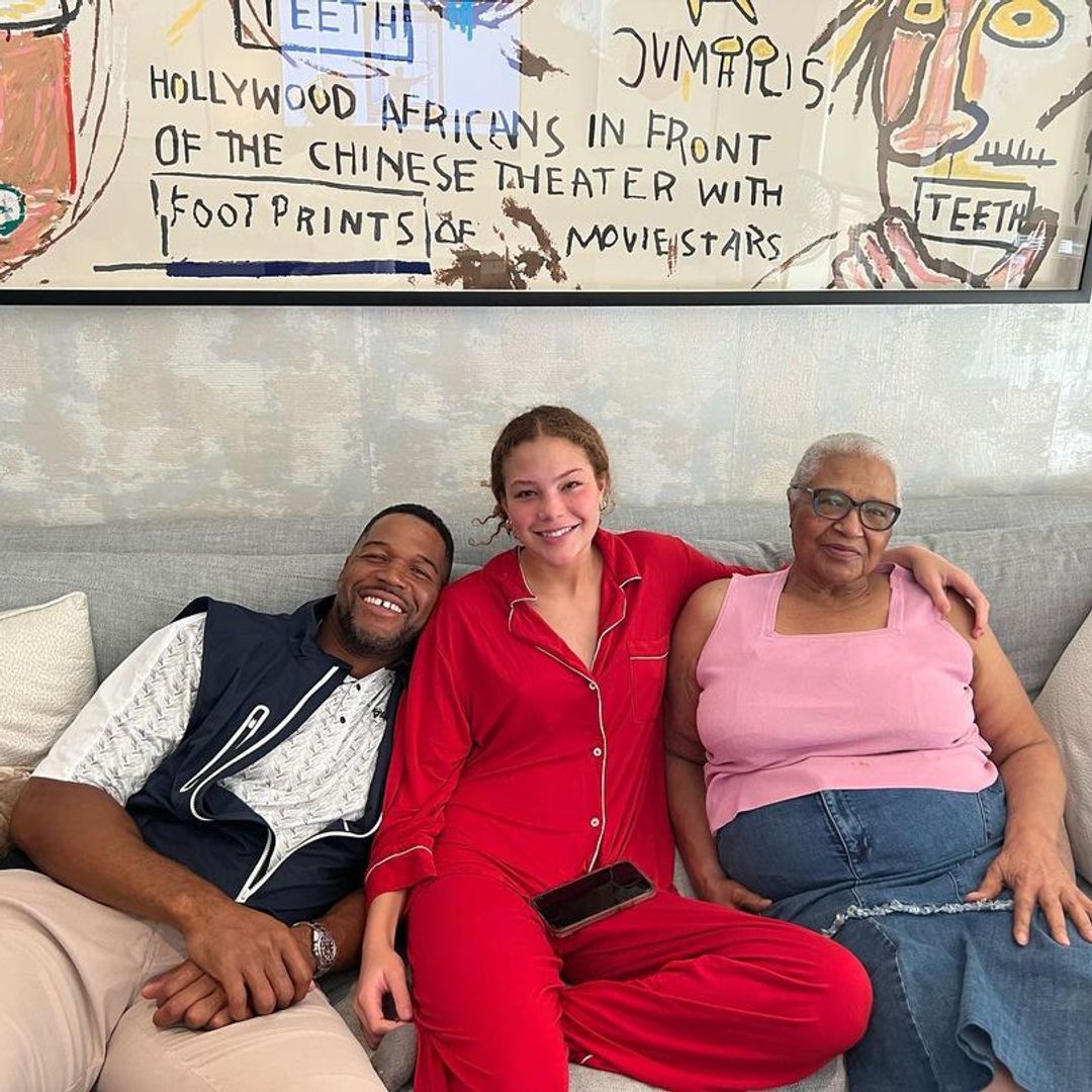Michael Strahan sat on a couch with his daughter and his mom to his left, all are smiling wide