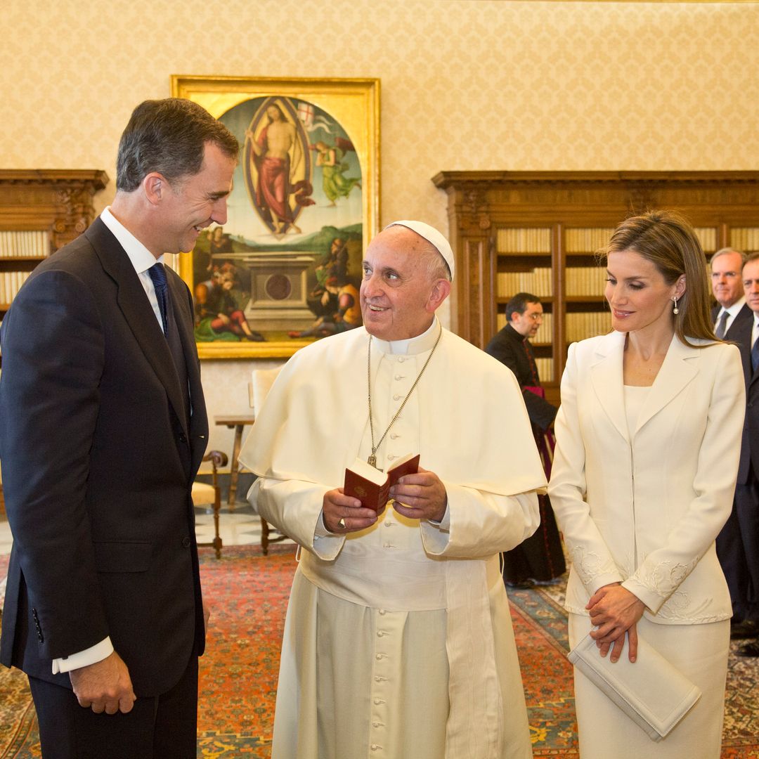 Queen Letizia of Spain with the Pope in the Vatican City. The Pope wears traditional white robes and Queen Letizia wears a white skirt suit and matching clutch bag.