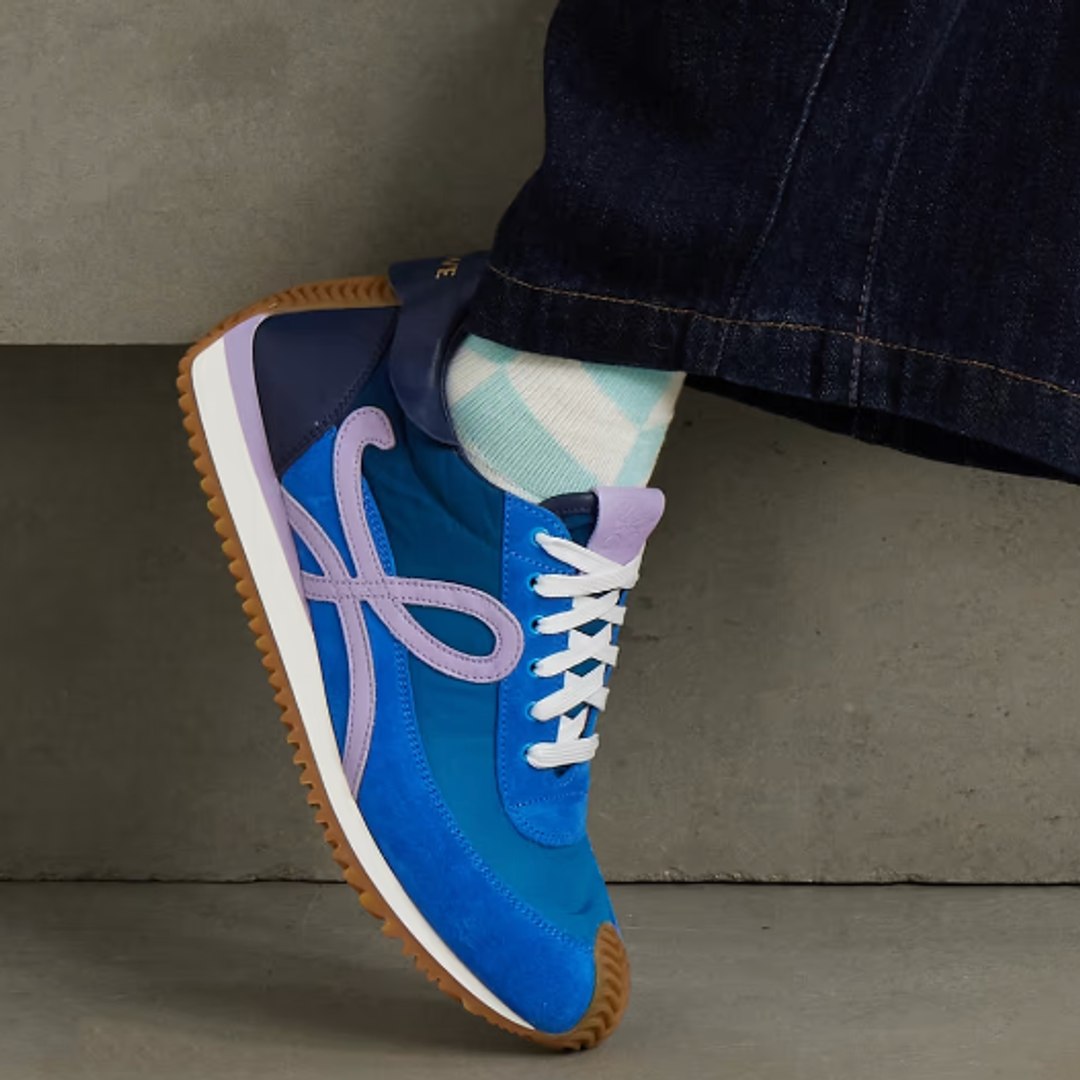 A model wears a pair of blue, lilac and navy Loewe 'Flow Runner 2.0' trainers with jeans and mint green socks