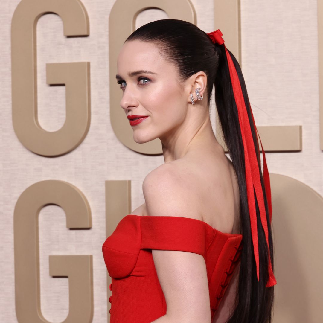 Rachel Brosnahan looking over her shoulder at the Golden Globes with her hair in a red bow and red lipstick 