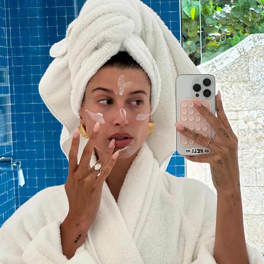 Hailey Bieber in a dressing gown and towel applying face cream