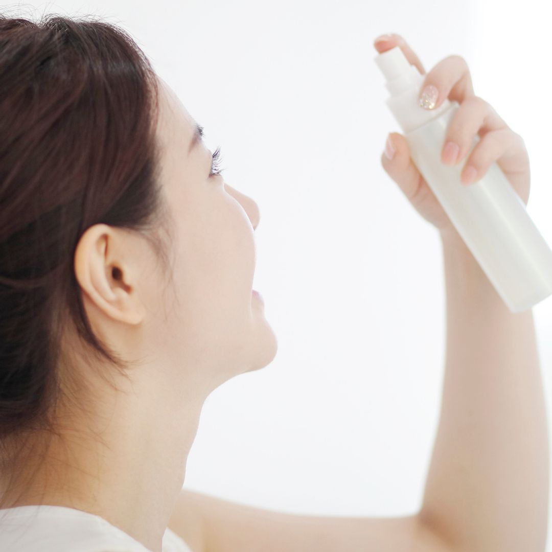 Young woman spraying setting spray for makeup on face