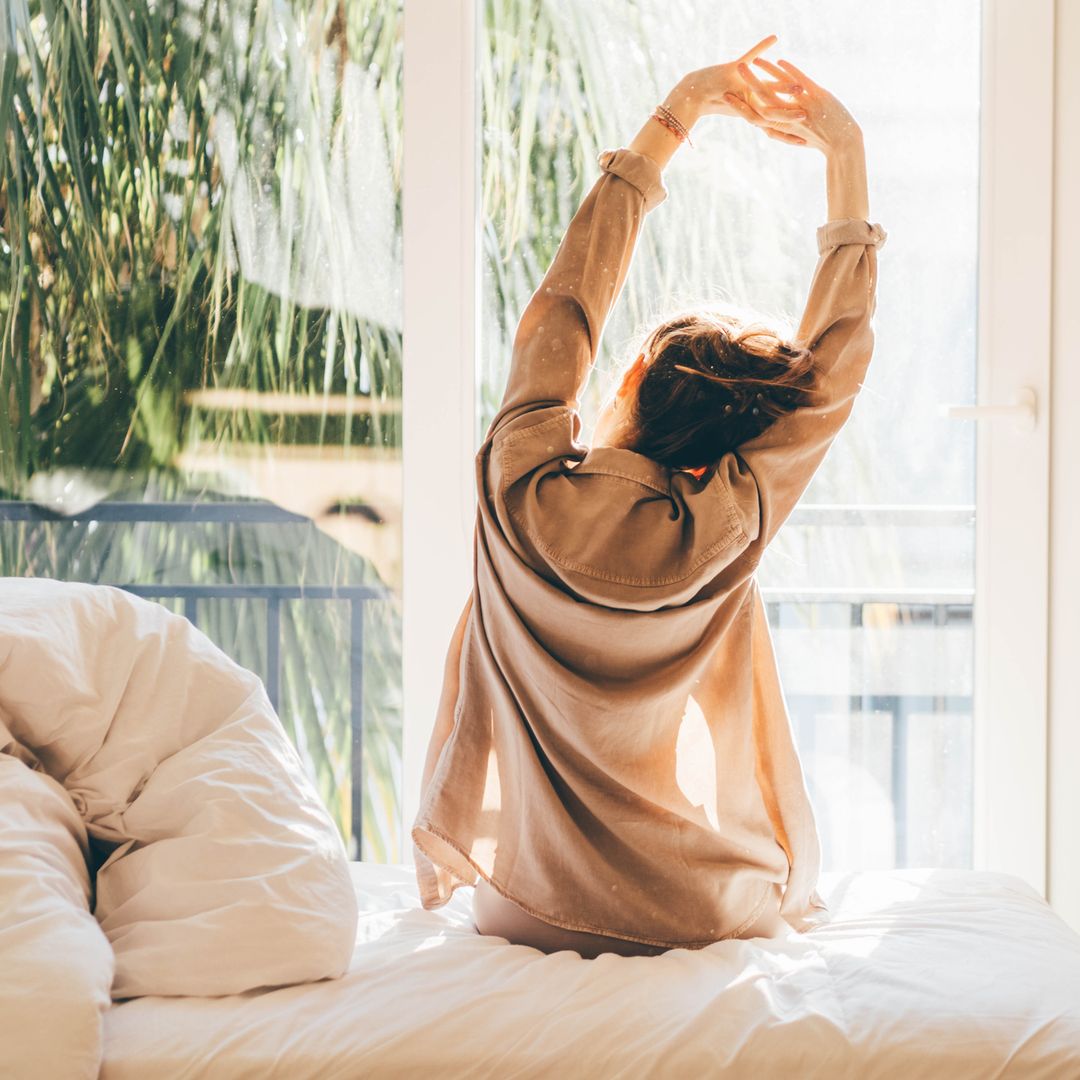 Woman waking up and relaxing near window at home.