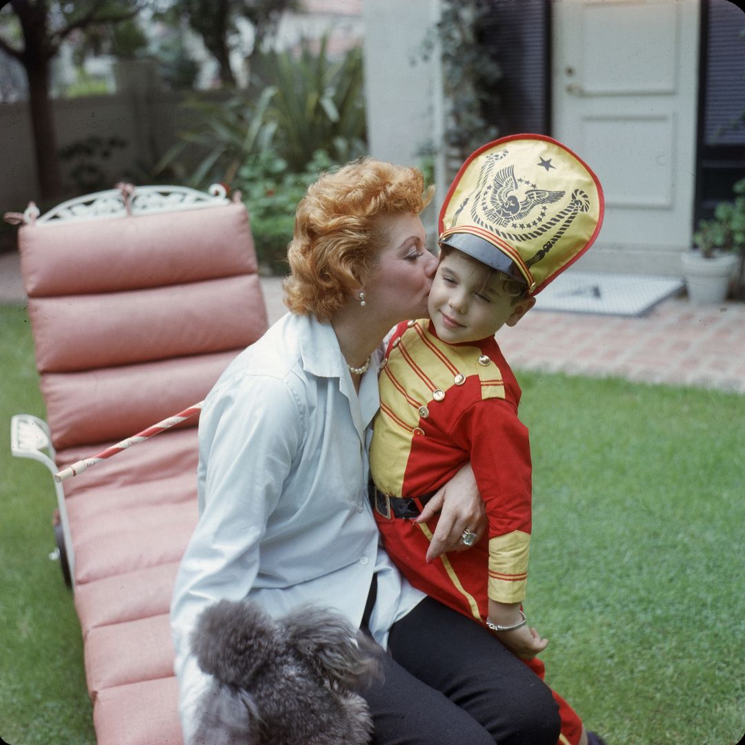 American actress and comedienne Lucille Ball (1911 - 1989) kisses her son Desi Arnaz Jr, who is dressed as a drum major with a baton, in the back yard of their home, Los Angeles, California, late 1950s.