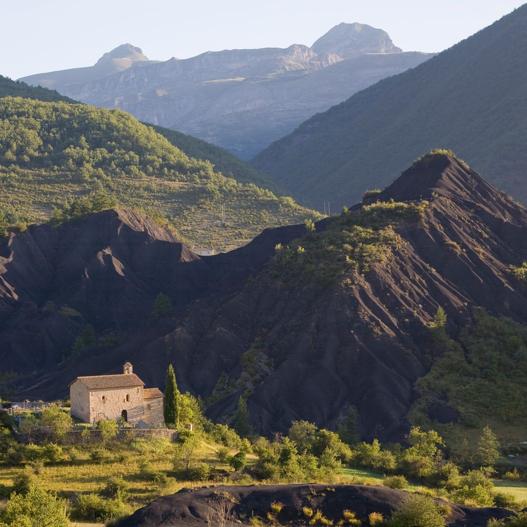 A view of some green and rocky fields and mountains with a small rustic house at their foot