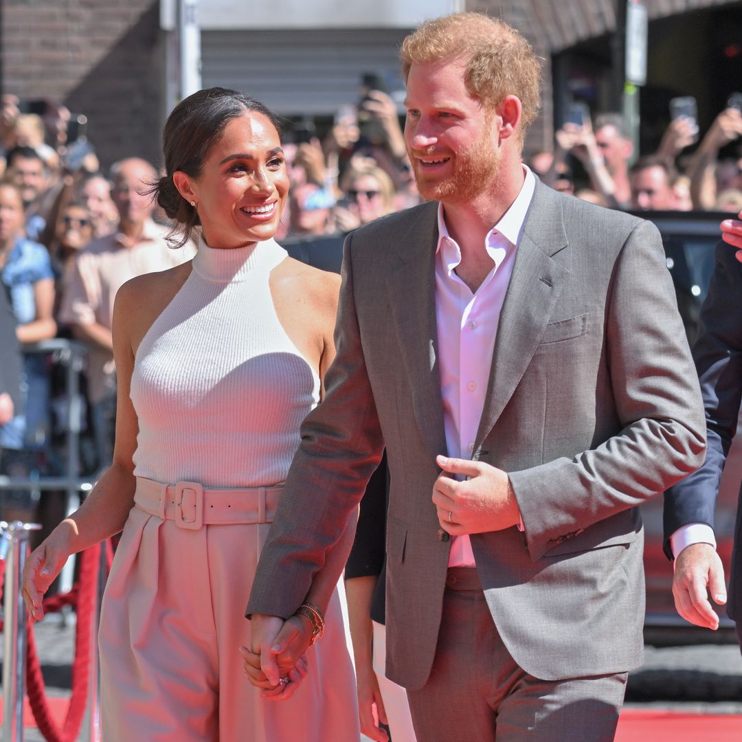 Prince Harry and Meghan smiling on a red carpet