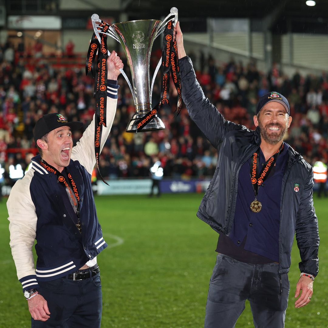 Ryan Reynolds and Rob McElhenney holding the National League trophy and smiling wide