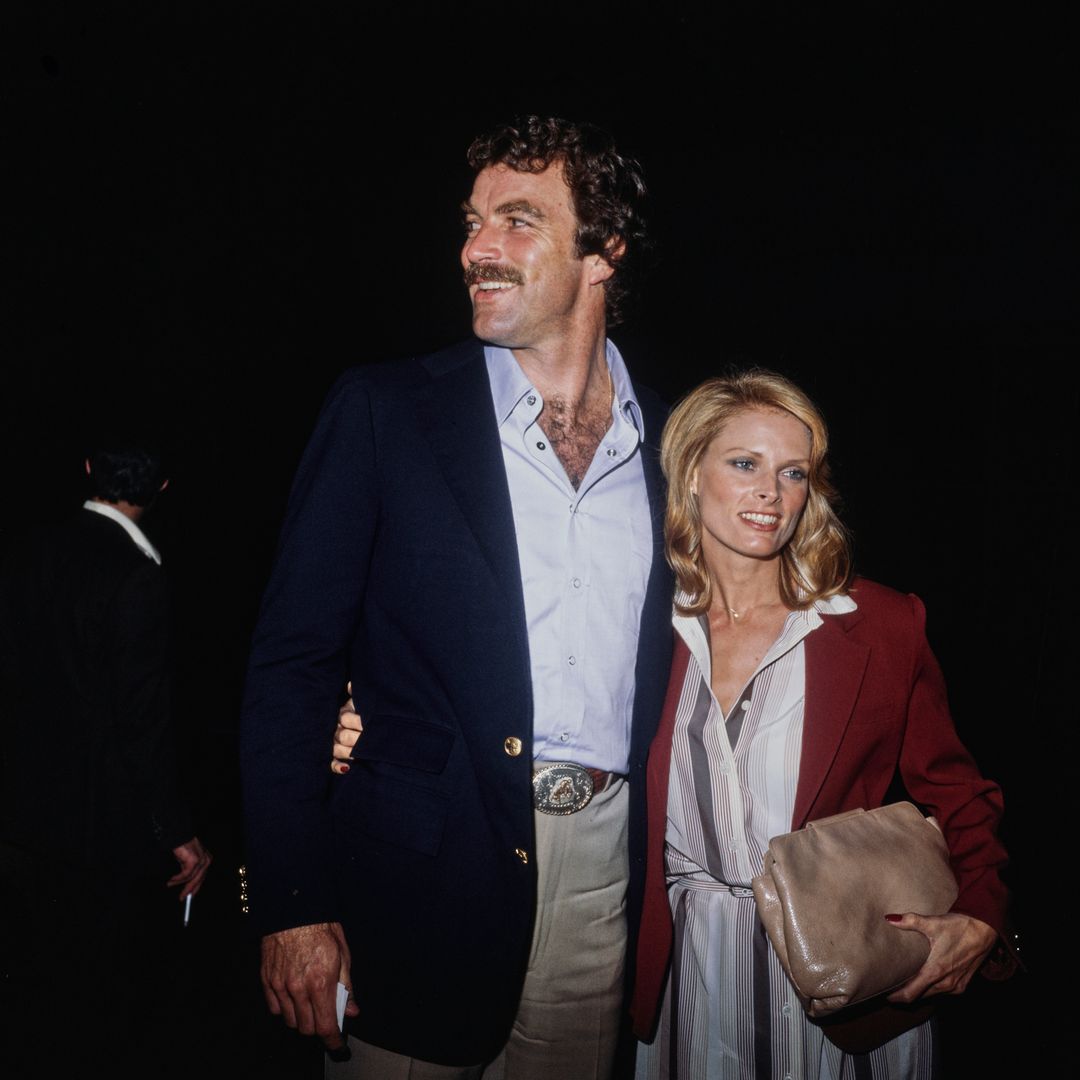 American actor Tom Selleck, wearing a dark blue blazer with brass buttons over a white open collar shirt, and his wife, American actress and model Jacqueline Ray, who wears a red jacket over a striped dress, at Mr Chow's Restaurant in Beverly Hills, California, circa 1980
