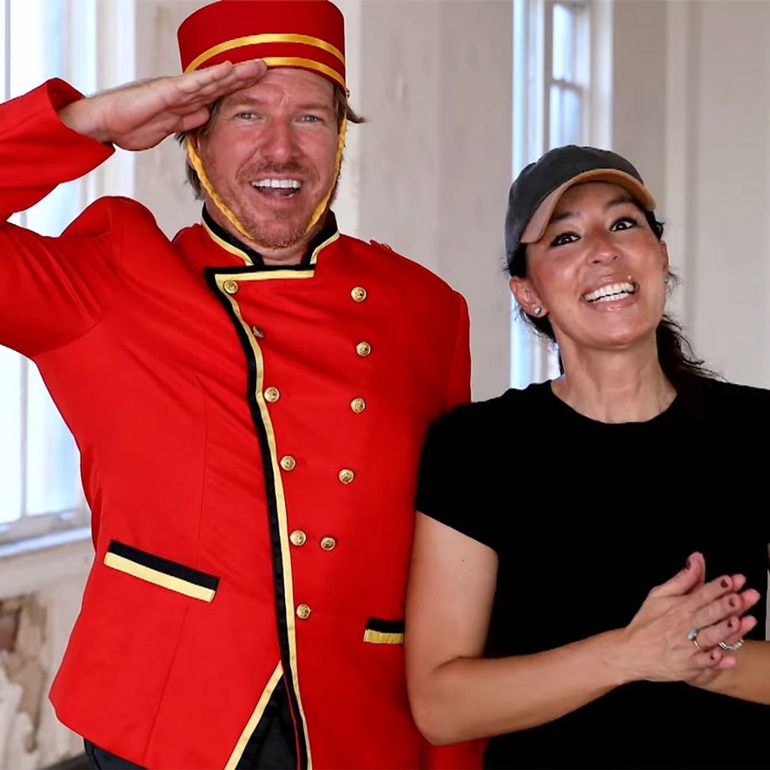 Chip Gaines in a porter uniform standing next to Joanna Gaines in a black tee in an empty romotel