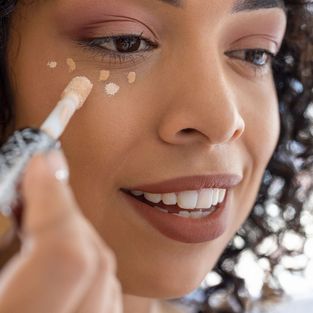 woman applying peach color correcting concealer.