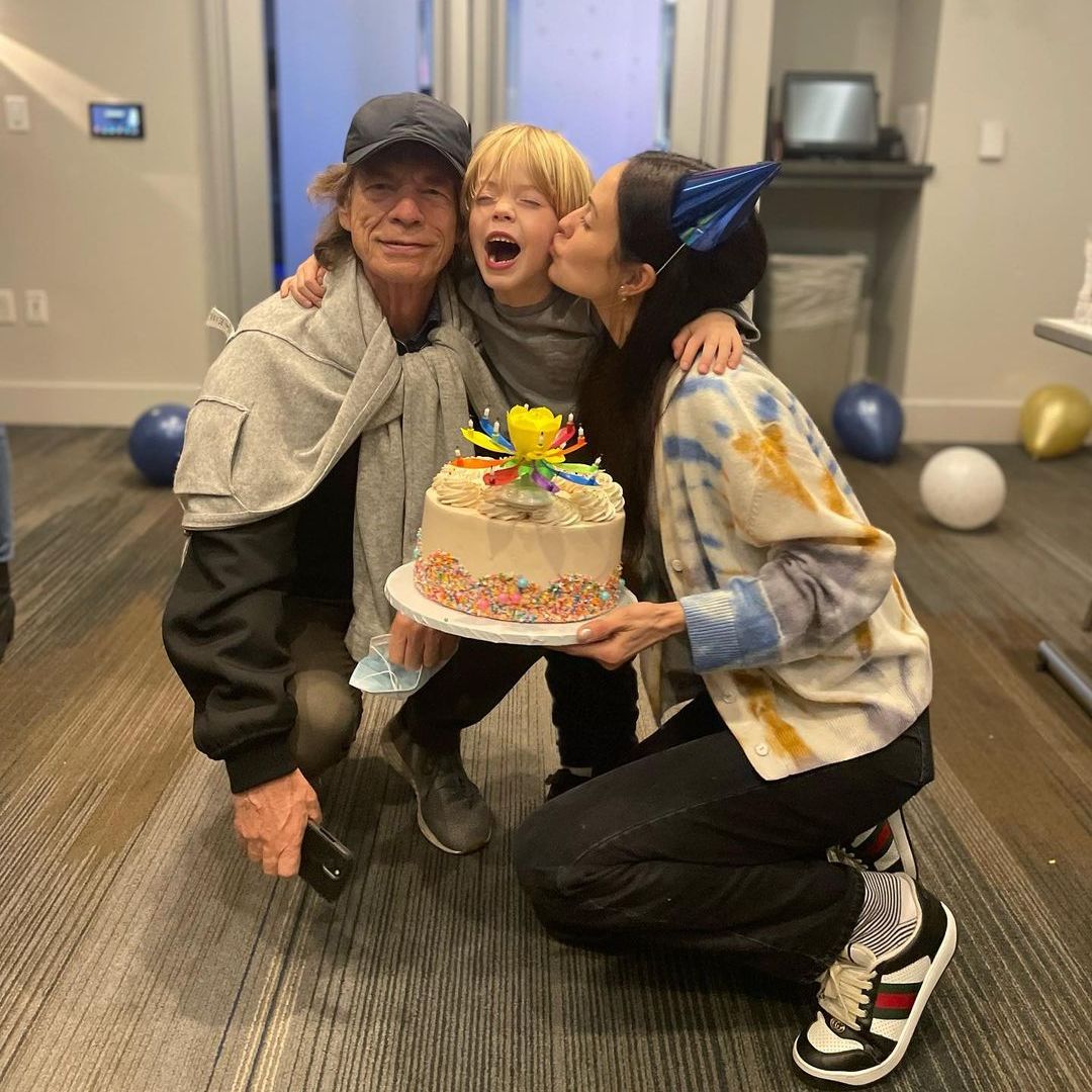 Mick and Melanie crouching down to hug their son, smiling, and holding a birthday cake