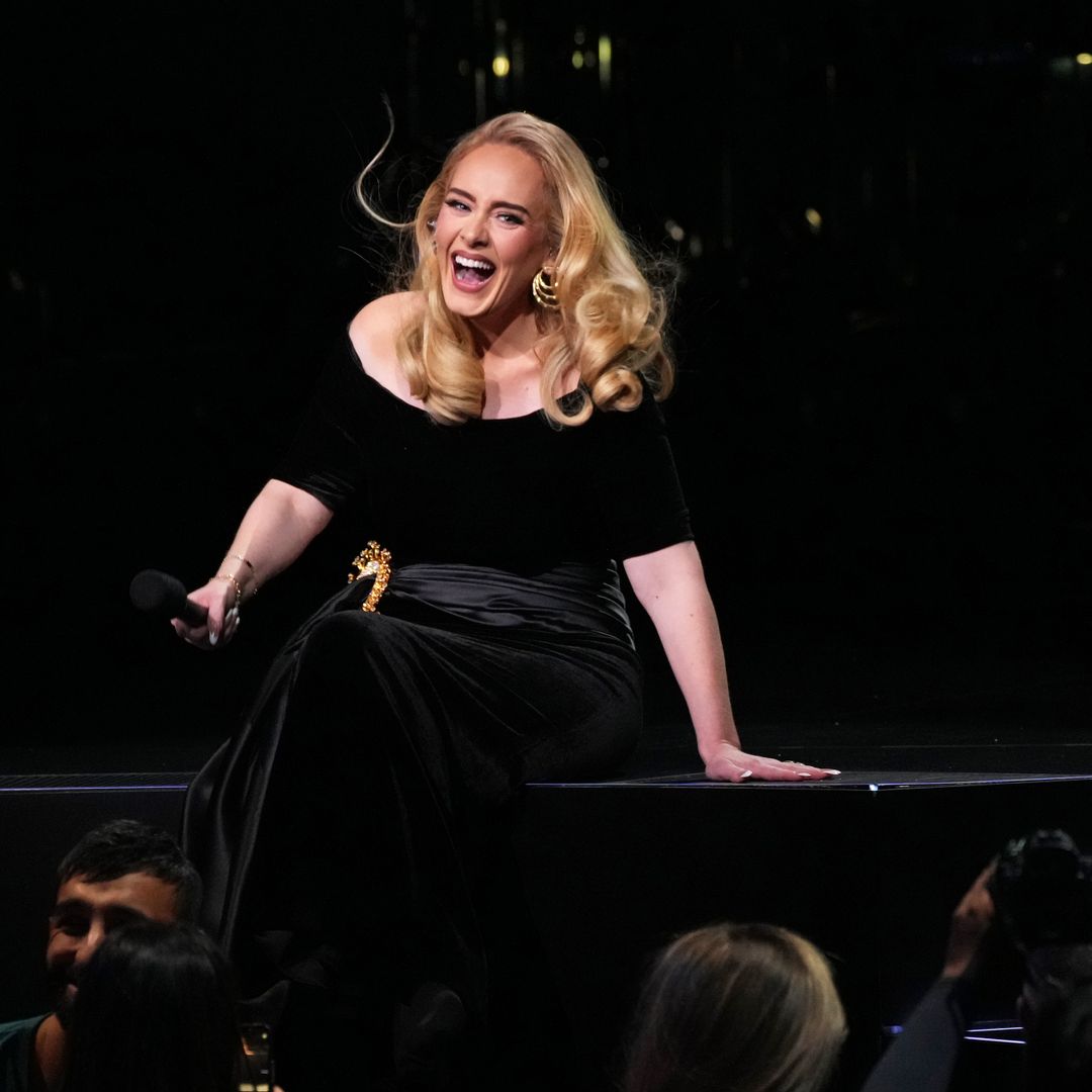 Adele at her Las Vegas residency smiling wide while sat on the edge of her stage