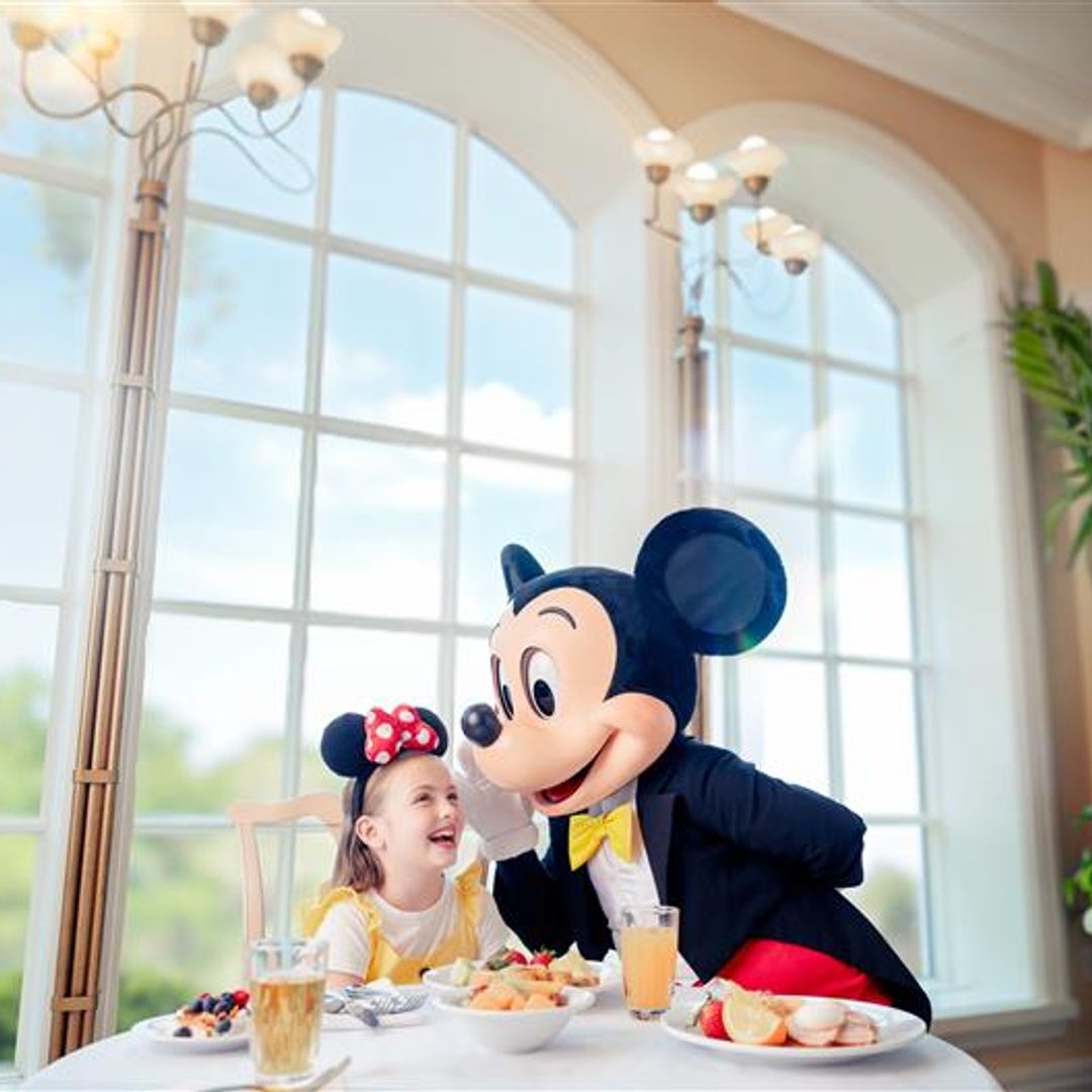 young girl wearing mickey mouse ears speaking to mickey mouse character in Disney hotel
