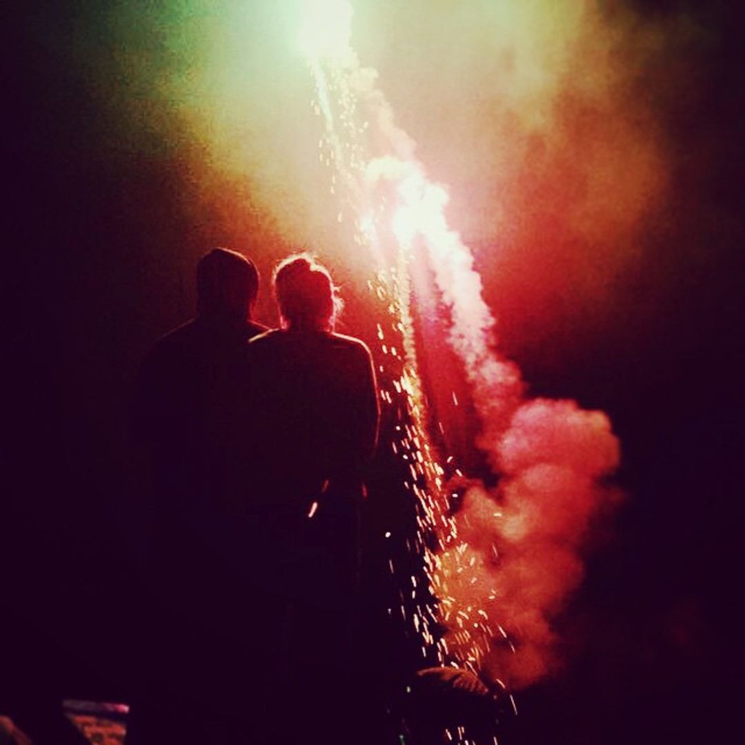 Margot and Tom silhouetted by the light of a red firework