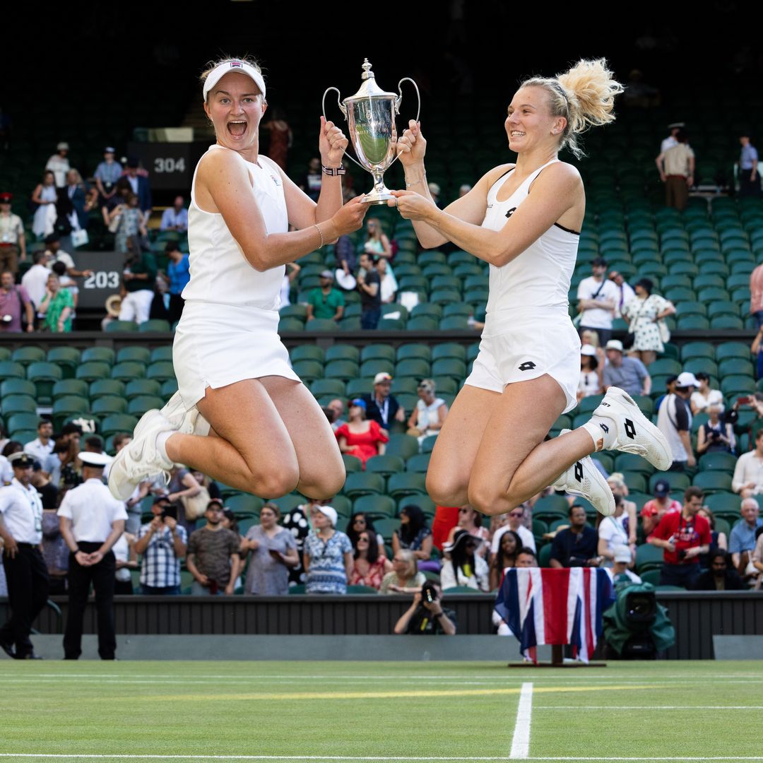 Barbora Krejcikova and Katerina Siniakova smiling holding a cup together and jumping in the air
