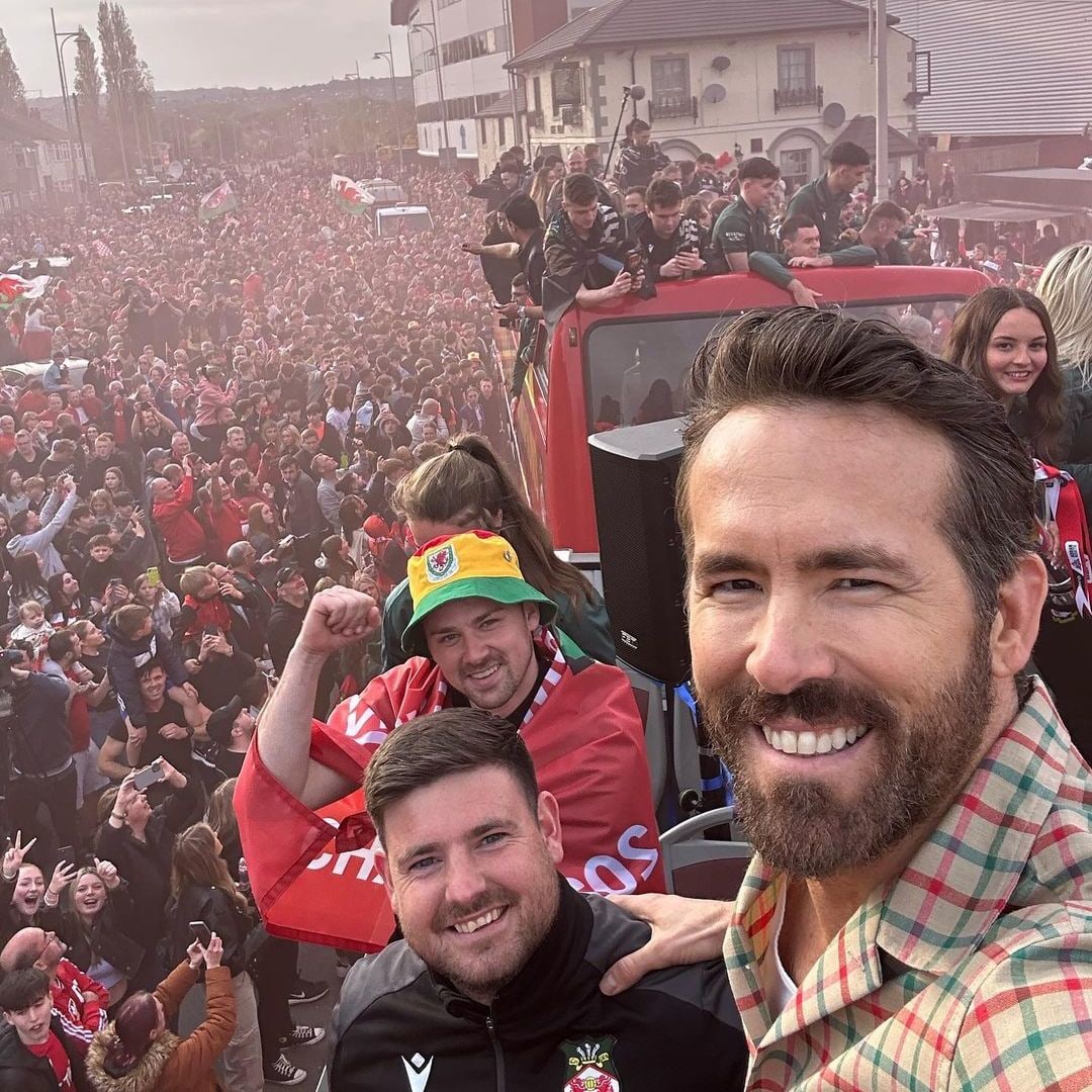 Ryan smiling in a selfie taken on top of a bus with hundreds of fans in red celebrating around it