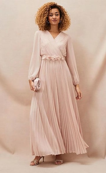 Pink pleated maxi dress with long sleeves and flower detailing at waist