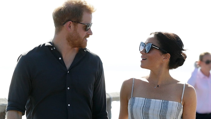 Prince Harry and Meghan Markle smiling at each other in sunglasses