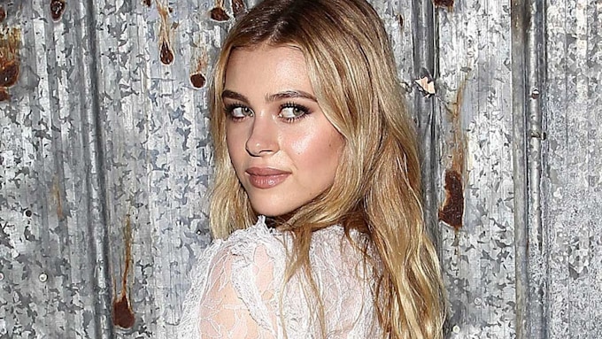 Nicola Peltz wearing a white lace dress looking over her shoulder
