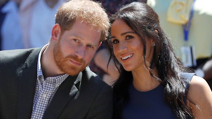 Meghan Markle in blue whispering to Prince Harry in a suit