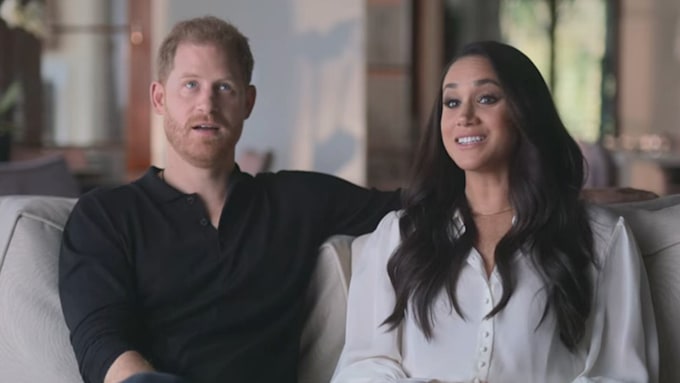 Prince Harry and Meghan are sat smiling while on sofa